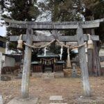 長野県下諏訪町にある御作田神社の正面写真。しめ縄と紙垂（しで）が飾られた年季の入った石鳥居の奥に、歴史を感じさせる木造の小さなお社が建っている。周囲には大きな木が茂り、落ち葉が広がる静かな境内の風景。