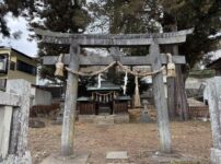 長野県下諏訪町にある御作田神社の正面写真。しめ縄と紙垂（しで）が飾られた年季の入った石鳥居の奥に、歴史を感じさせる木造の小さなお社が建っている。周囲には大きな木が茂り、落ち葉が広がる静かな境内の風景。